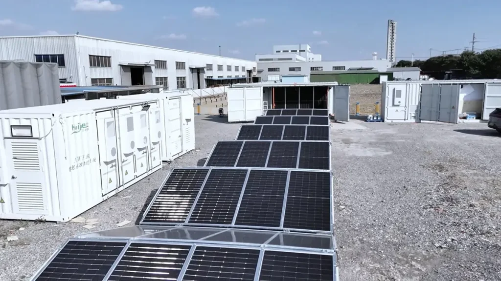 Unbranded fold-out solar container with photovoltaic panels deployed on a level gravel worksite A deployed fold-out solar container creates a larger generating surface than the container roof alone.
