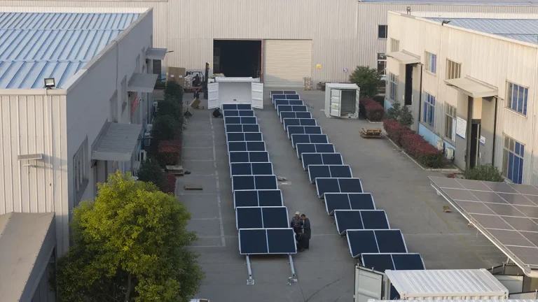 Contêiner solar dobrável genérico sobre uma base nivelada de cascalho ao lado de uma estrada de acesso e vala de drenagem em um local industrial remoto.
